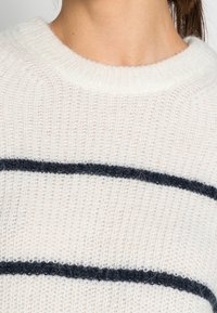 Pull ivoire à texture côtelée, avec des rayures horizontales bleu marine foncé. Col rond, matière tricotée douce et design décontracté.