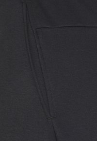 Pantalon de jogging bleu marine en tissu doux et texturé, avec une poche latérale visible et une couture décorative.