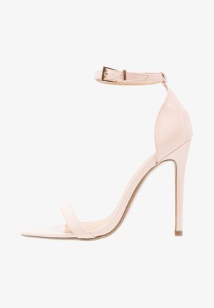 Beżowy sandał na wysokim obcasie z lakierowanej skóry, z paskiem wokół kostki, szpiczastym noskiem i pojedynczym paskiem z przodu. Charakteryzuje się gładką, połyskującą fakturą.