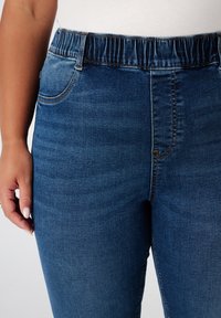 Jean en denim ajusté, couleur bleu clair, taille élastique et poches latérales. Tissu texturé avec des détails de décoloration subtils.