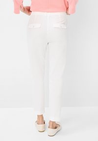 Witte broek met een slim fit, voorzien van twee achterzakken met kleppen en knopen. De stof heeft een gladde textuur en een subtiele glans.