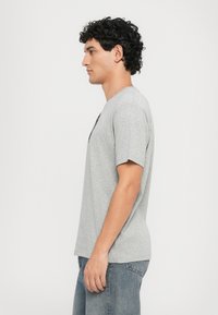Tricou gri cu mânecă scurtă dintr-un material moale și texturat. Dispune de un gât rotund și o vedere laterală cu o croială confortabilă.