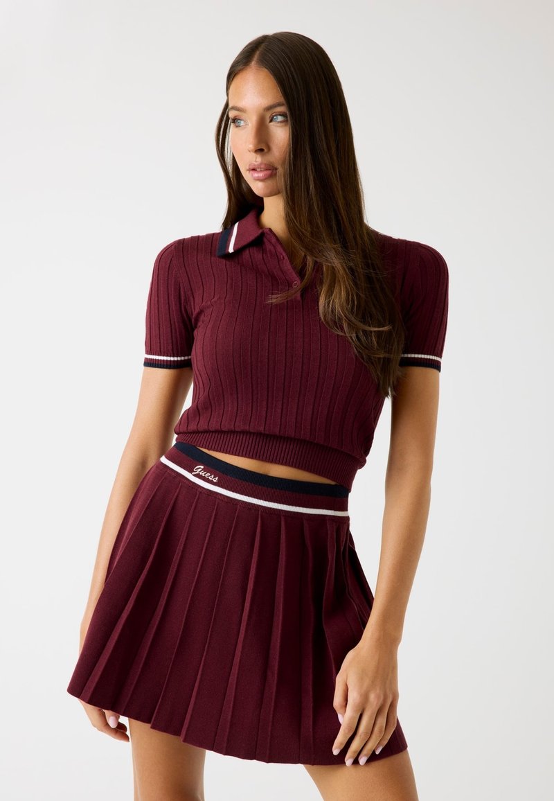 Bordó kötött crop polo, gallérral és bordázott textúrával; párosítva egy matching pliszírozott szoknyával, amely márkázott derékpánttal rendelkezik.
