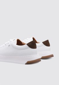 Baskets blanches en cuir avec des accents en suède marron au niveau du talon, surface texturée, bout rond, lacets blancs et semelle en caoutchouc. Design décontracté.