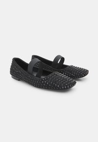 Zapatos planos negros de ante, con puntera redonda, suela de goma y tachuelas decorativas negras en la parte superior. Tira elástica en el empeine.