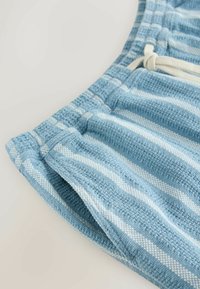 Shorts en tissu texturé à rayures bleues et blanches avec une taille élastique et un nœud de cordon blanc, affichés en gros plan sur un fond neutre.