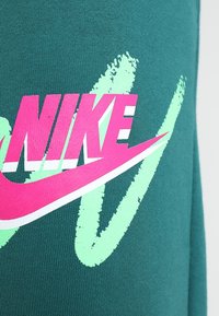 Grön tyg med en stor rosa "Nike"-logotyp med en swoosh i vitt och neongröna accenter. Slät struktur med djärv grafisk design.