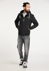 Jachetă neagră cu fermoar, cu glugă, având accente galbene și șnururi. Purtați cu blugi gri și adidași bleumarin cu șireturi albe.