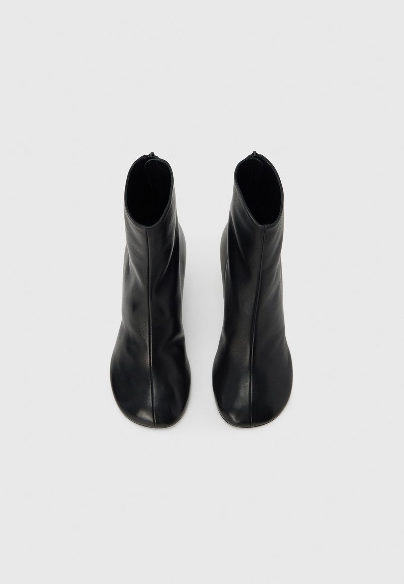 Bottes basses en cuir noir avec une texture lisse, un embout arrondi et un design minimaliste. Fermeture éclair à l'arrière.