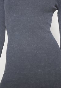 Långärmad klänning i mörkgrå ribbad tyg, med en figurnära design. Texturen visar vertikala ränder och subtila prickar.