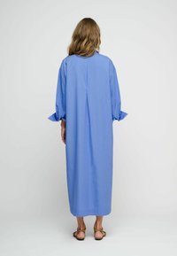 Abito lungo e leggero in cotone blu chiaro, con una linea dritta, maniche lunghe con polsini arrotolati e un dettaglio di cucitura sul retro.