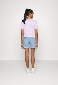 T-shirt lilás de manga curta, combinada com calções de riscas finas azul-claro. Modelo a usar sapatilhas brancas com detalhes em tons pastel e meias amareladas.