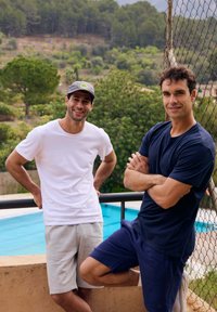 Dwaj mężczyźni stoją blisko basenu. Jeden ma na sobie białą koszulkę i szare szorty; drugi nosi granatową koszulkę i pasujące szorty. W tle widać zielone drzewa.