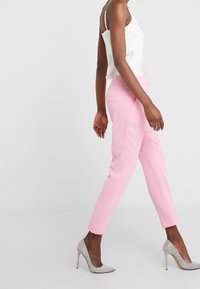 Rosa skräddarsydda byxor med smal passform, ankellängd och fickor, kombinerade med en vit sidentopp och silverfärgade stilettklackar.