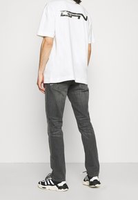 White cotton t-shirt with black graphic print on the back, paired with gray jeans and black and white sneakers. Casual outfit, minimal design.