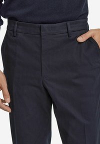 Marineblaue Fischgrät-Hosen mit flachem Vorderteil, Gürtelschlaufen und Seitentaschen, aus strukturiertem Stoff gefertigt.