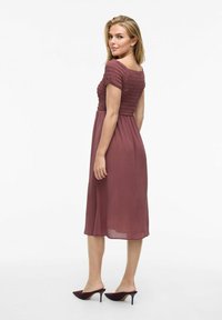 Robe midi de couleur framboise avec un corsage smocké, des manches courtes et une jupe fluide, associée à des mules à talons hauts à bout pointu.