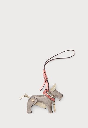 Porte-clés en cuir en forme d’un petit chien avec un collier rose et une boucle de suspension sur un fond blanc uni.