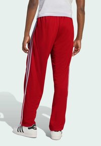 Rote Sporthosen aus strukturiertem Mesh-Stoff mit weißen Seitenstreifen. Getragen mit weißen Sneakers, die schwarze Akzente aufweisen.