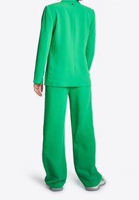 Zielony, dopasowany garnitur z długimi rękawami i spodniami o szerokich nogawkach, wykonany z gładkiej tkaniny, z zapięciem na guziki z tyłu marynarki.
