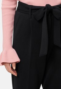 Czarne, dopasowane spodnie z paskiem do wiązania, połączone z różowym prążkowanym swetrem z rozszerzanymi mankietami. Gładka faktura i strukturalny krój.