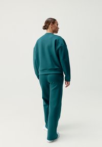 Teal sweatshirt och matchande byxor gjorda av ett slätt tyg. Designen har en avslappnad passform, ribbade ärmslut och en rundad halsringning.