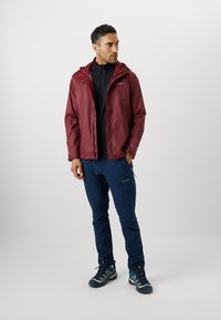 Bordeauxfarbene wasserdichte Jacke mit Kapuze, schwarzes Innenfutter, blaue Hose und graue Schuhe mit türkisfarbenen Akzenten; funktionales Design, leichte Materialien.