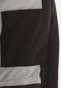 Schwarzer und grauer Jackenstoff mit einer markanten schwarzen Tasche und einem horizontalen grauen Streifen. Glatte Textur mit Nahtdetails.