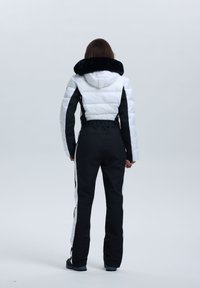 Gepolsterte Skijacke in Weiß und Schwarz mit einem Kragen aus Kunstfell, taillierter Passform und kontrastierenden Seitensch Stripes an den schwarzen Hosen.