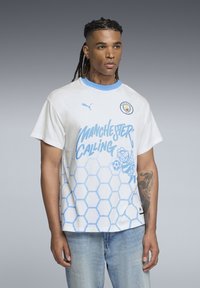 Cămașă albă din bumbac cu accente albastre și un model în fagure. Prezintă textul "Manchester Calling" și un grafic cu o albină. Gât rotund și mâneci scurte.