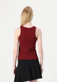 Burgundy ribbed tank top with a scoop neck, sleeveless design, and a fitted silhouette. Paired with a pleated black mini skirt.