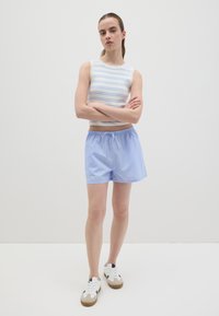Gestreiftes, kurzes Tanktop in Weiß und Hellblau, kombiniert mit hellblauen Nadelstreifen-Shorts mit elastischem Bund und Kordelzug. Weiße Sneakers.