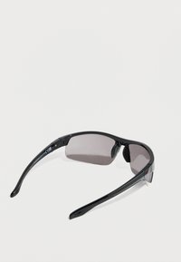 Μαύρα γυαλιά ηλίου με κομψό σχέδιο, με γκρι φακούς, λαστιχένιες εσοχές στη μύτη και ευέλικτους μαύρους βραχίονες. Σήμανση CE ορατή στο σκελετό.