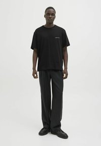 Sort bomulds T-shirt med afslappet pasform, korte ærmer og små hvide tekstdetaljer på brystet. Sammen med løstsiddende sorte bukser og sko.