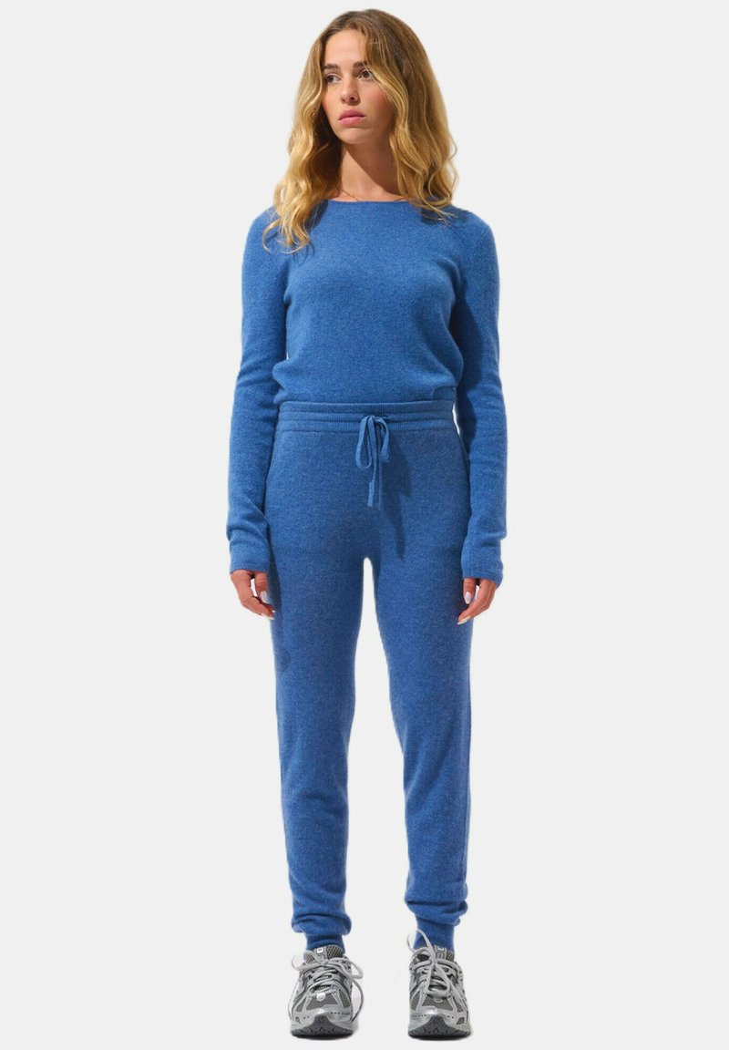 Blå stickad loungedress med långa ärmar och byxor med dragsko. Mjuk textur med ribbade avslut. Bärs med gråa träningsskor.