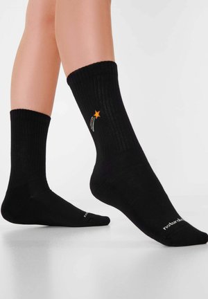 Zwarte sok met geribbelde textuur, voorzien van een geborduurde oranje ster en slepende lijnen. Enkel lengte met logo op de zool.