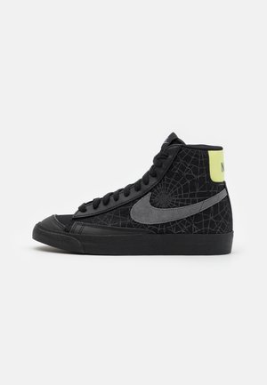 Black high-top sneakers with textured mesh material, featuring a grey swoosh logo, black sole, and a neon yellow accent on the heel.
