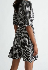 Eine Frau trägt ein schwarz-weiß gestreiftes Kleid mit Puffärmeln und einem gerafften Saum, aus der Rück- und Seitenansicht gezeigt.