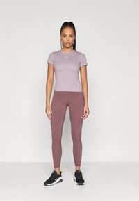 Top corto de lavanda claro con mangas cortas y leggings ajustados color marrón, ambos hechos de tela elástica. Zapatillas deportivas negras completan el atuendo.