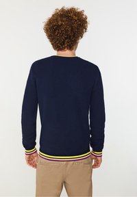 Mörkblå stickad tröja med långa ärmar, med en rund halsringning och färgglad randig ribbad nederkant i gult, rött och vitt.