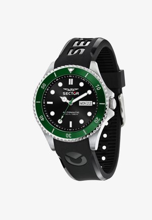 Montre automatique noire avec un boîtier en acier inoxydable, une lunette verte et un bracelet en silicone noir. Elle présente un cadran noir, des index horaires blancs et un affichage de date.