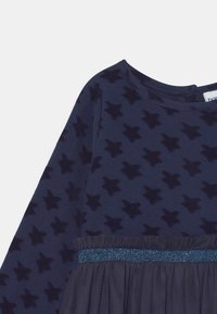 Vestido de color marino con mangas largas; presenta un estampado de estrellas, una cinturilla azul brillante y una sección inferior texturizada. Tejido suave, escote redondo.