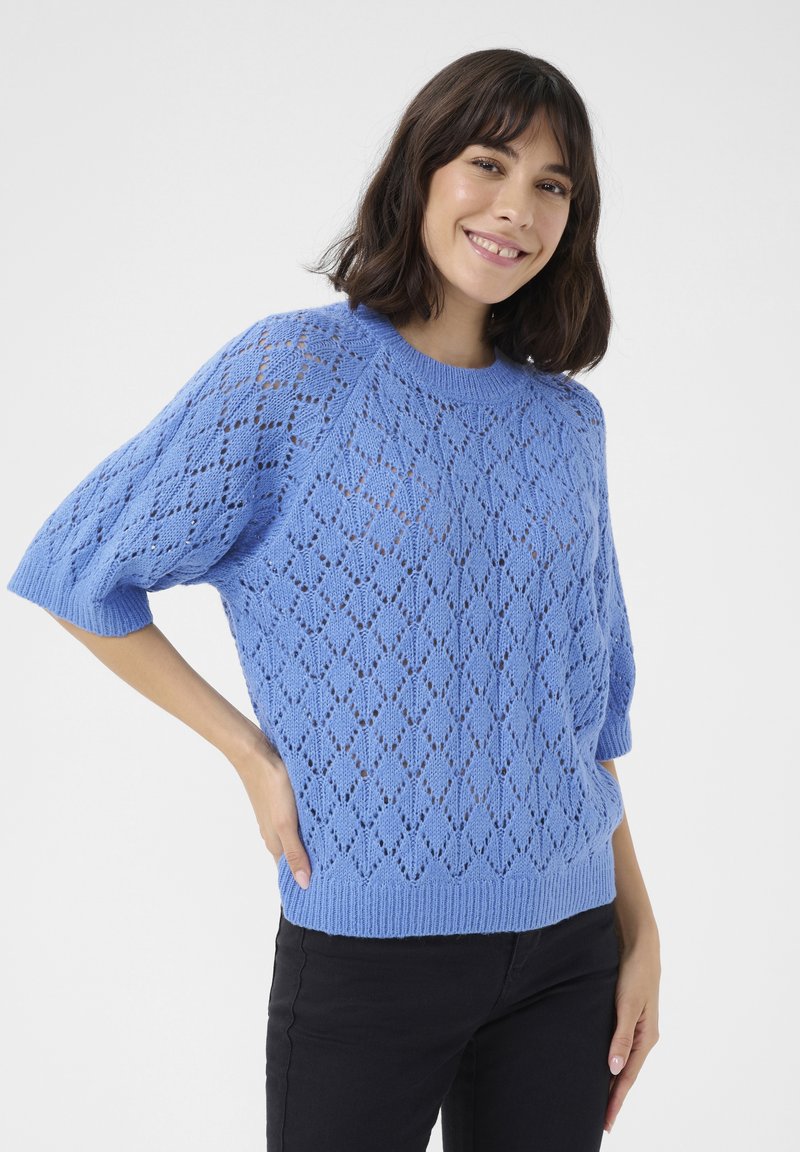 Pull en tricot bleu clair avec un motif en losange, manches courtes et ourlet côtelé. Associé à un pantalon noir.