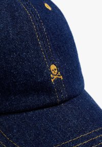 Căciulă din denim cu o nuanță de albastru închis, cusături galbene și un mic detaliu brodat cu craniul și oasele încrucișate în galben pe lateral.