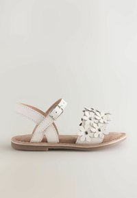 Sandalo bianco con decorazioni floreali, cinturino alla caviglia regolabile, soletta morbida simile al camoscio e suola in gomma marrone chiaro.