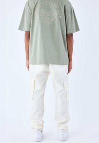 Olijfgroen T-shirt met korte mouwen met een hartontwerp op de rug, gecombineerd met crèmekleurige cargobroek met zijzakken en witte sneakers.