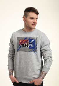 Sudadera gris con un estampado gráfico colorido de un coche con acentos rojos y azules. La tela tiene una textura suave y puños acanalados.