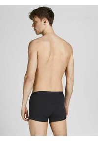 Schwarze Baumwoll-Trunk-Unterwäsche, die von hinten an einer Person präsentiert wird, mit einem weichen Bund und einer engen Passform. Einfaches, glattes Design.