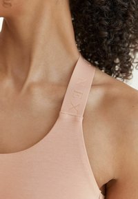 Helle rosa Sport-BH mit breiten Trägern, geprägt mit Logo, glatter Textur und runder Ausschnitt für eine figurbetonte Passform.
