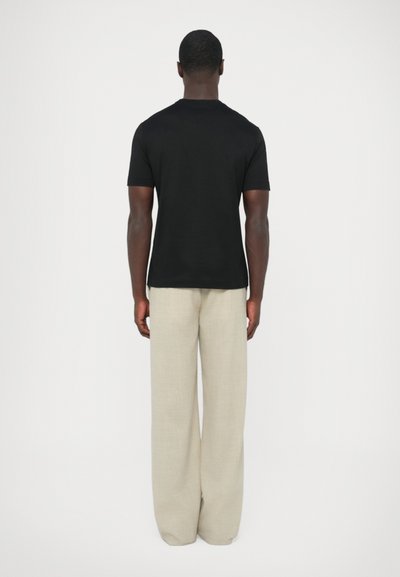 Čierne tričko s krátkym rukávom a okrúhlym výstrihom, doplnené širokými béžovými nohavicami, pohľad zozadu na bielom pozadí.
